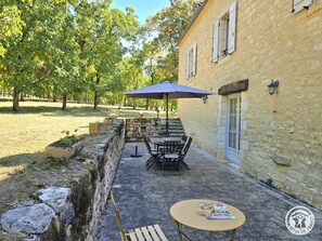 An outdoor patio area with stone walls, a table with chairs, and a blue umbrella.