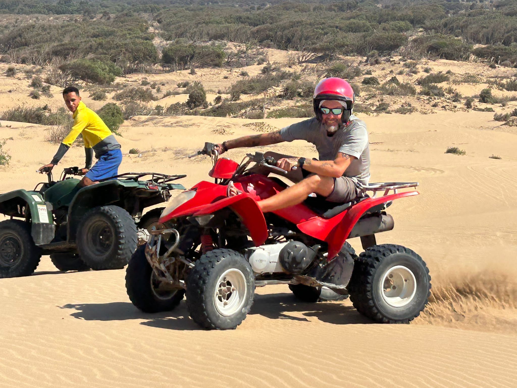 Dos personas manejando cuatrimotos en un paisaje desértico.