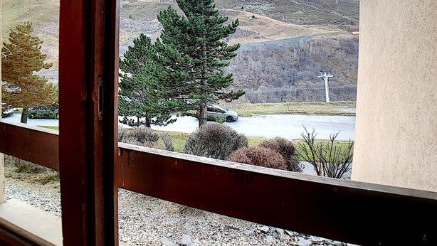 Une vue depuis une fenêtre à cadre en bois, donnant sur un parking où sont garées quelques voitures, une chaîne de montagnes et un poteau électrique.