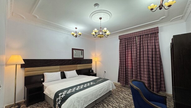 A hotel room with a large bed, a desk, a chair, a chandelier, and a window with curtains. - Eqamh Etlala Quba- إقامة إطلالة قباء (Madinah)