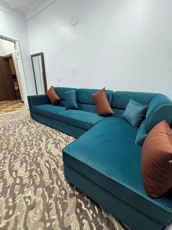 A teal sectional sofa with brown cushions in a room with patterned carpet and white walls. - Eqamh Etlala Quba- إقامة إطلالة قباء (Madinah)