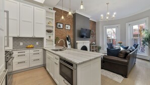 A modern kitchen with white cabinetry, a central island, and a brick accent wall. - 2 Bed Luxury Condo in South End near Restaurant Row, (Boston)
