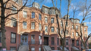 A row of red brick apartment buildings with multiple windows and balconies, a clear sky, and a street with parked cars. - 2 Bed Luxury Condo in South End near Restaurant Row, (Boston)