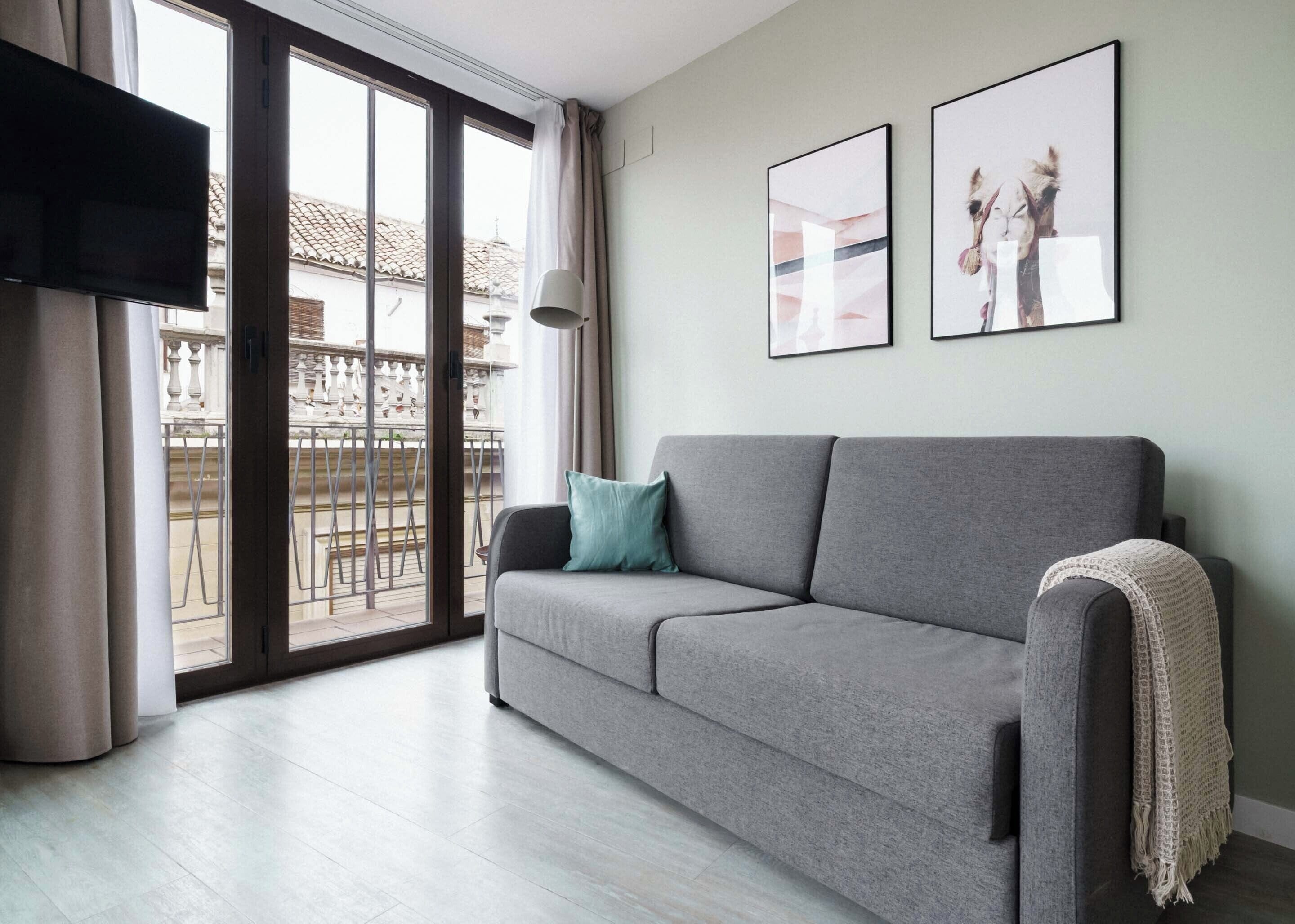 A modern living room with a grey sofa, a flat-screen TV, and a balcony with a railing.