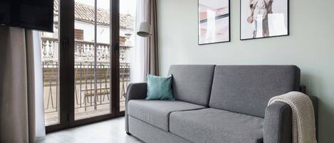 A modern living room with a grey sofa, a flat-screen TV, and a balcony with a railing.