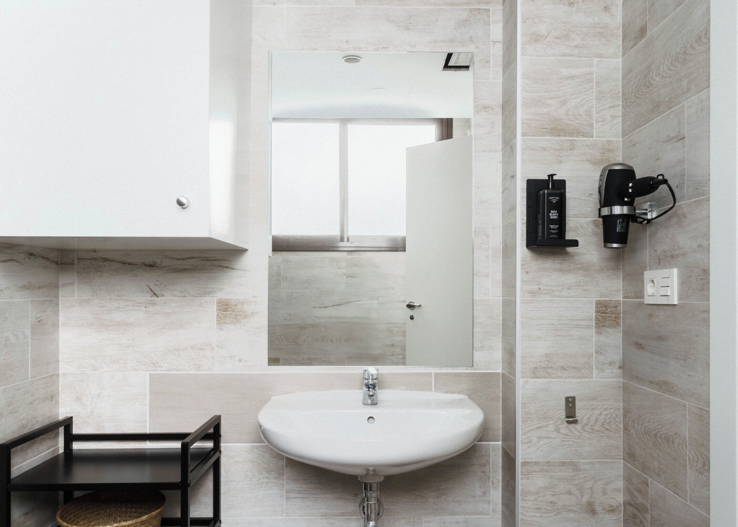 A modern bathroom with a white sink, a mirror, and a coffee machine on the wall.