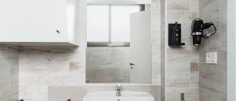 A modern bathroom with a white sink, a mirror, and a coffee machine on the wall.