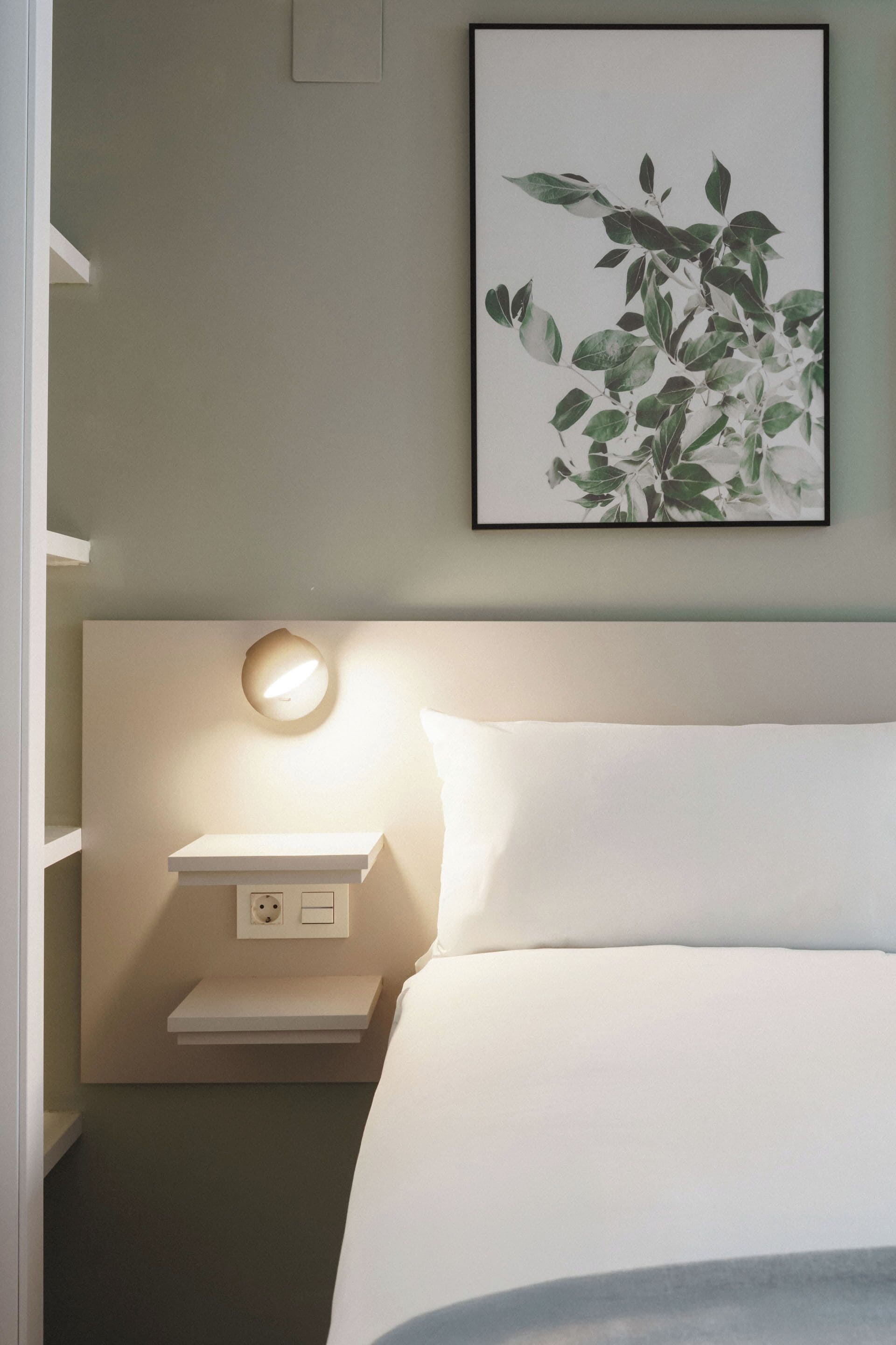 A neatly arranged bedroom with a bed, bedside table, and a wall-mounted light.
