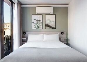 Ein Hotelzimmer mit einem großen Bett, zwei Nachttischen, einer Klimaanlage und zwei gerahmten Bildern an der Wand.