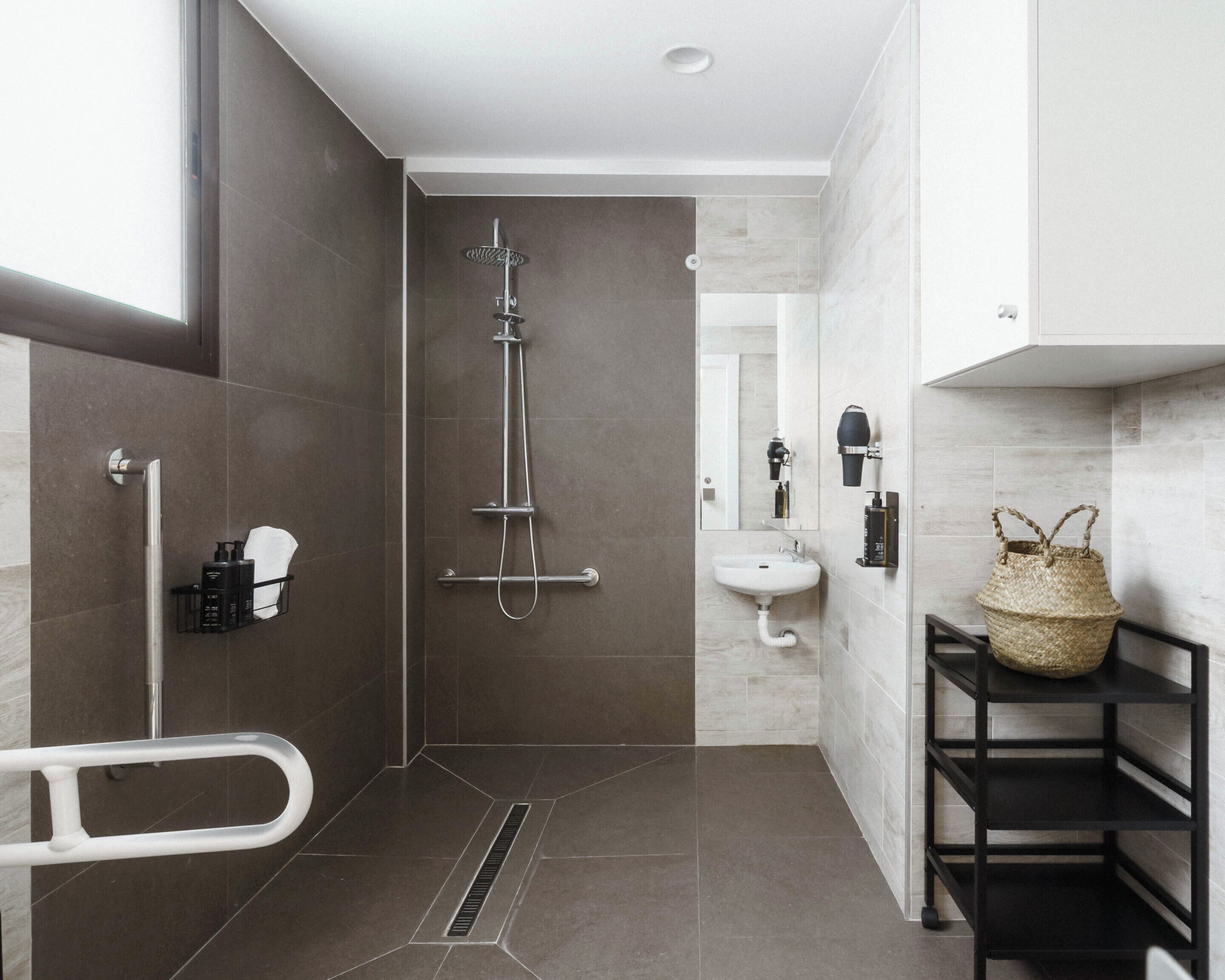 Une salle de bain moderne avec une douche à l’italienne, un lavabo blanc et une étagère noire sur laquelle repose un panier en osier.