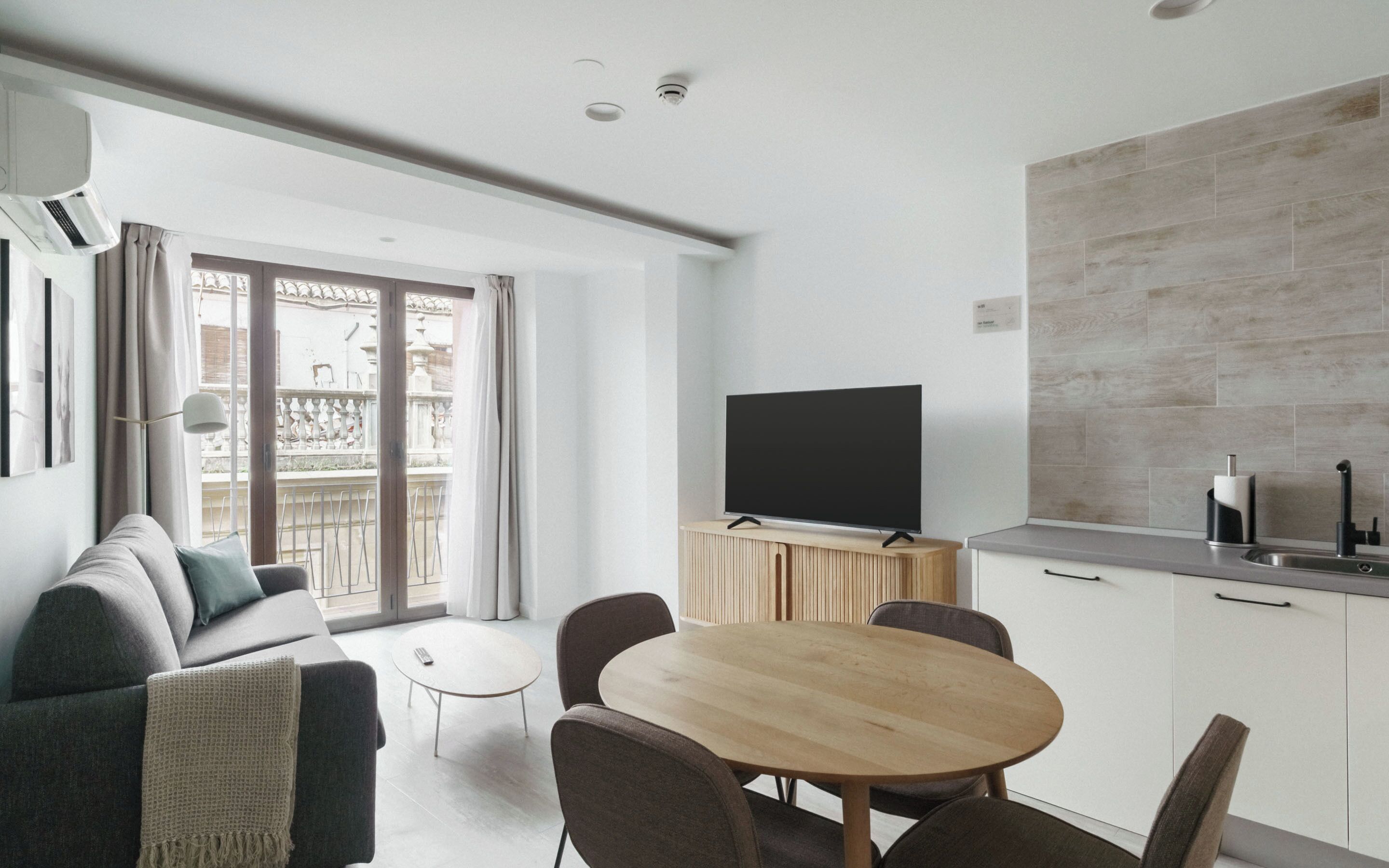 Una sala de estar moderna con un sofá, una mesa redonda de madera y un televisor de pantalla plana sobre un mueble de madera.