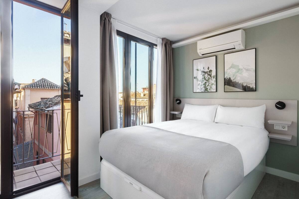 Una habitación de hotel con una cama grande, una puerta corrediza de vidrio a un balcón y dos cuadros en la pared.