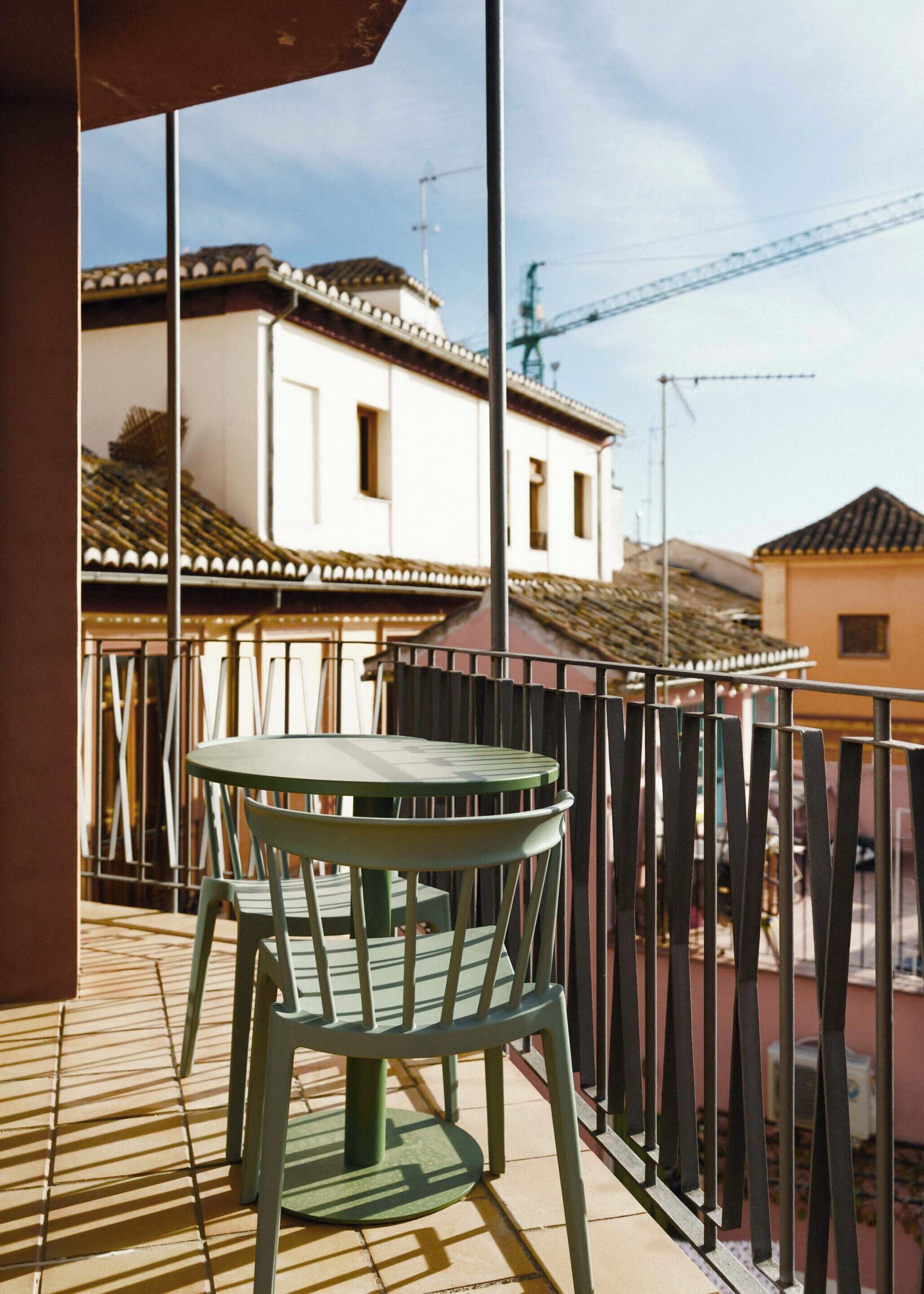 Un balcon avec une table et des chaises, donnant sur un quartier résidentiel avec des immeubles et une grue en arrière-plan.