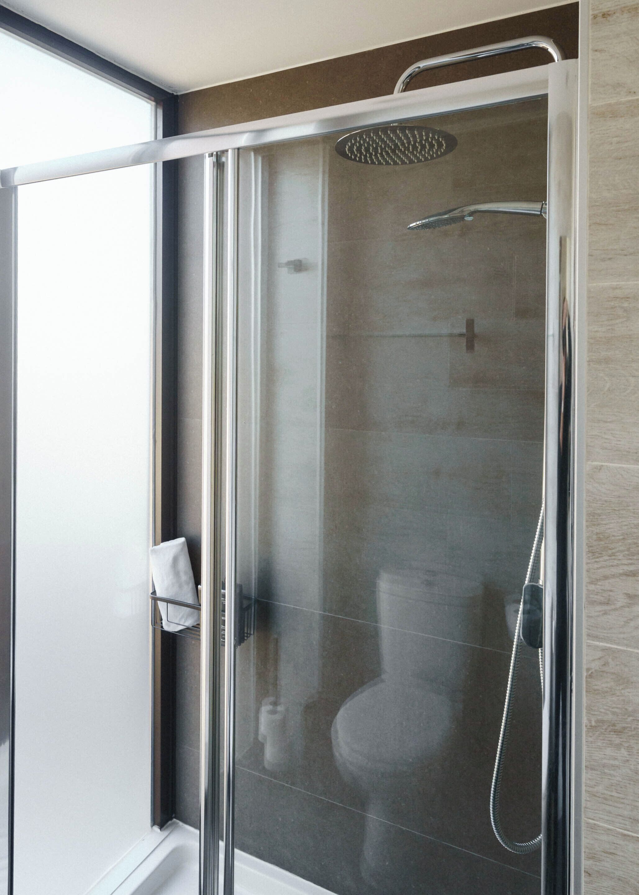 A modern bathroom with a glass-enclosed shower, a toilet, and a towel rack.