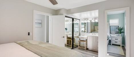 A bedroom with a bed, a ceiling fan, and a view into the bathroom.