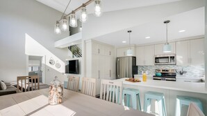 A modern kitchen with white cabinets, a stainless steel refrigerator, and a light blue island with stools. - Luxury Meets Coastal Charm in North Mission Beach (San Diego)