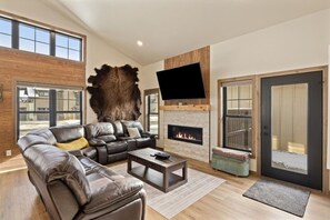 A modern living room with a leather sectional sofa, a stone fireplace, and a large TV mounted on the wall.