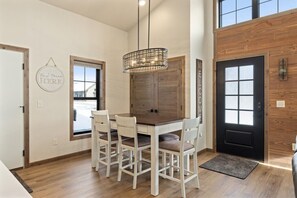 A dining area with a wooden table and four chairs, a hanging light fixture, and a door with a frosted glass panel.