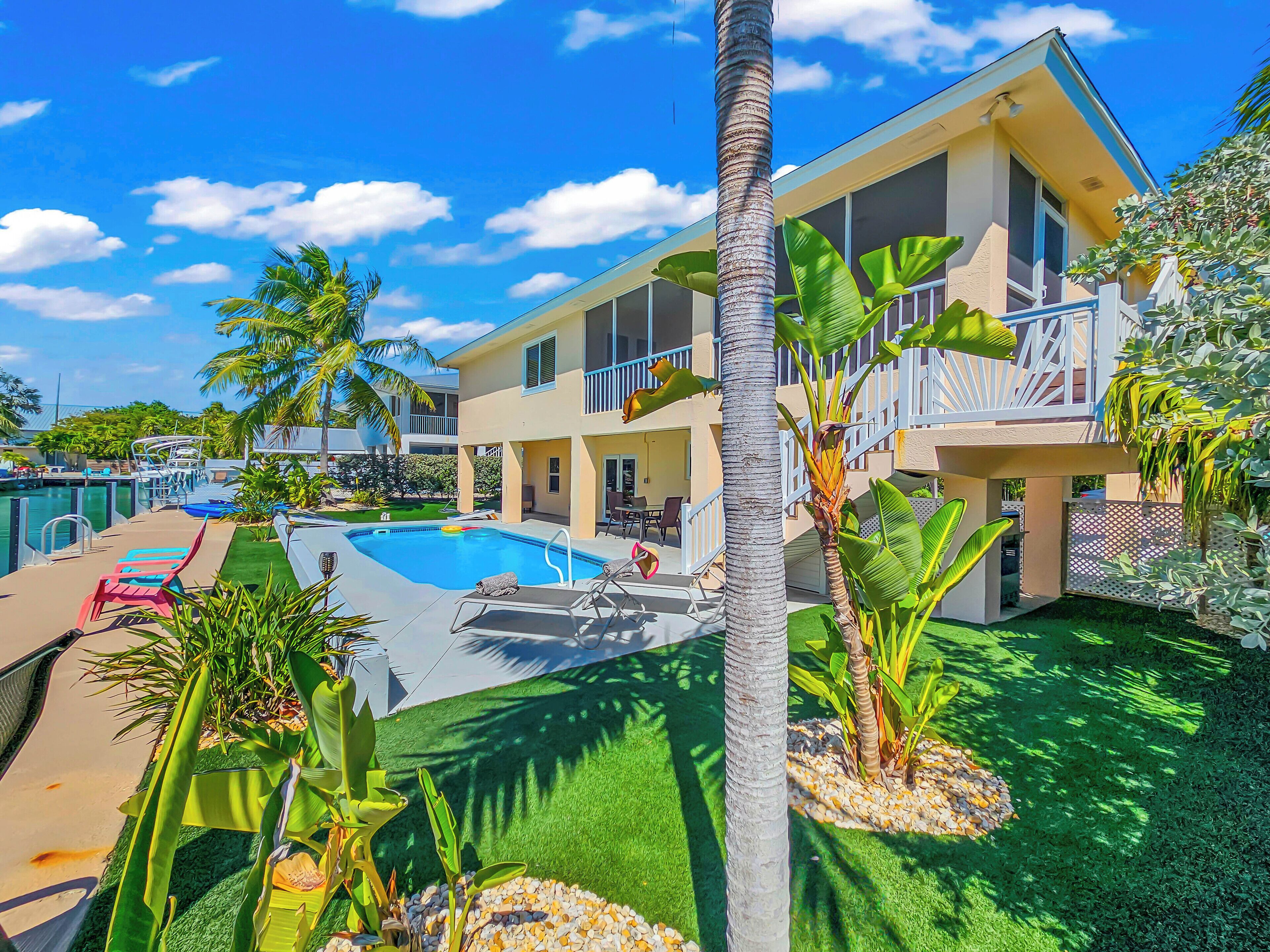 A pool area with lounge chairs, a clear blue sky, and a two-story building with balconies.