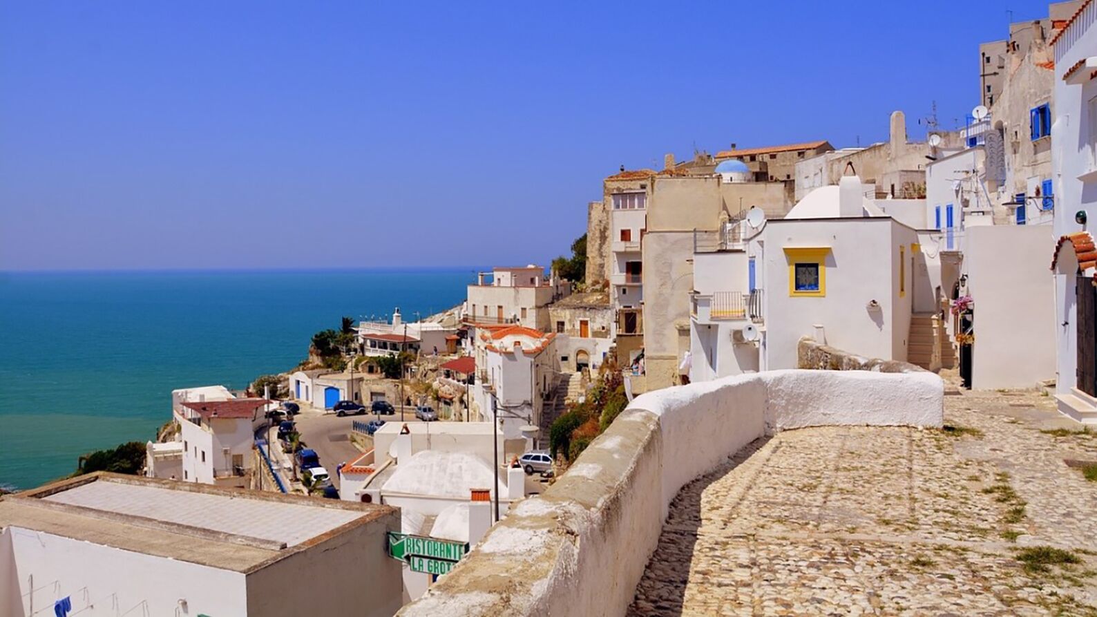 A coastal town with white buildings, a cobblestone path, and a clear blue sky.