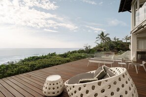 A wooden deck with outdoor furniture, a white woven chair, and a round table.