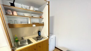 Una kitchenette compacta con un lavamanos, un refrigerador pequeño y repisas sobre la encimera con platos y vasos.