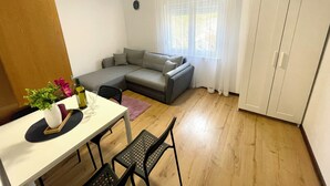 Una sala de estar pequeña y moderna con un sofá, una mesa de comedor con sillas y un armario blanco.