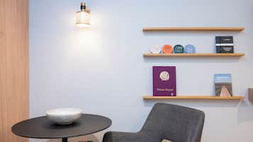 Quarto moderno com uma mesa redonda, uma tigela, uma cadeira e estantes com livros e objetos decorativos.