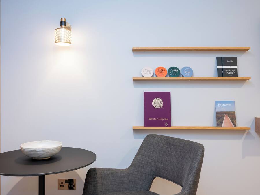 Quarto moderno com uma mesa redonda, uma tigela, uma cadeira e estantes com livros e objetos decorativos.