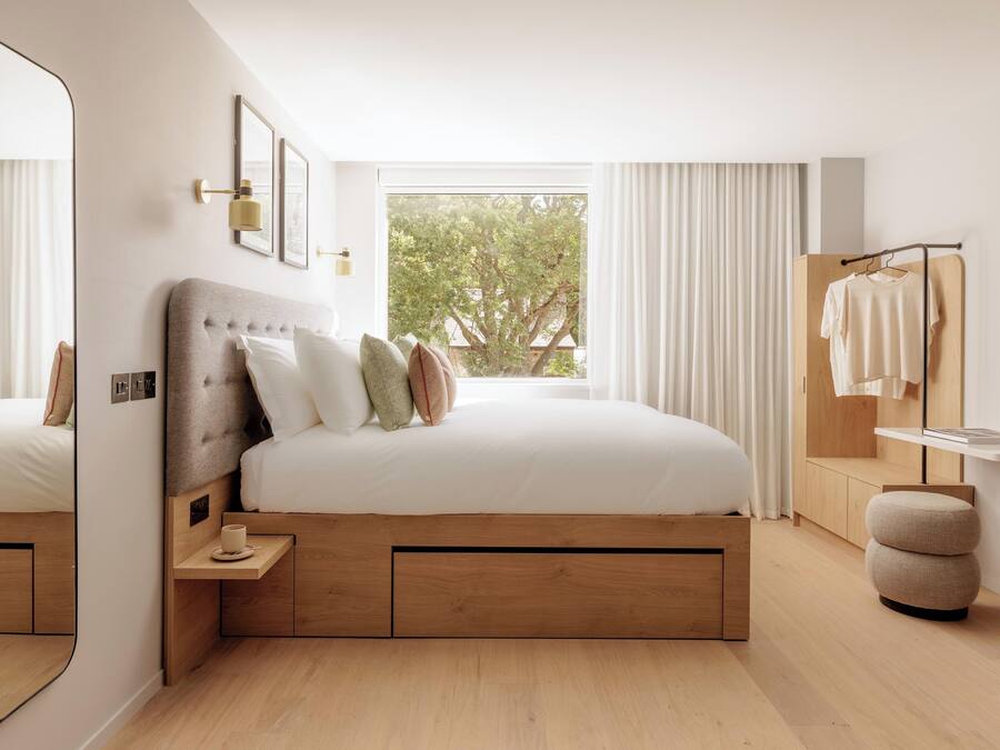 Un dormitorio moderno con una cama grande, una mesita de noche, un espejo y una ventana con cortinas.