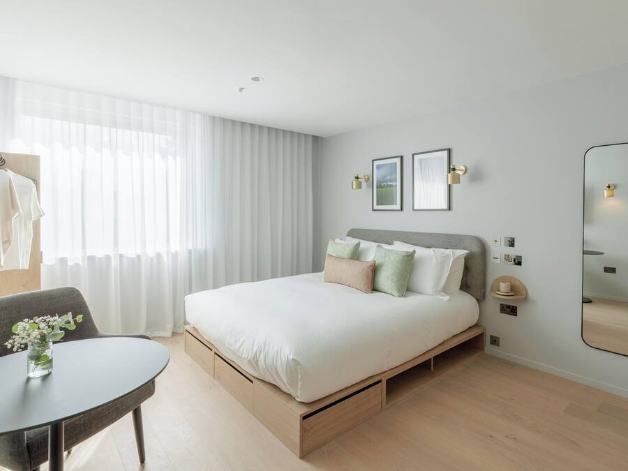 A modern bedroom with a bed, bedside tables, a chair, and a mirror.