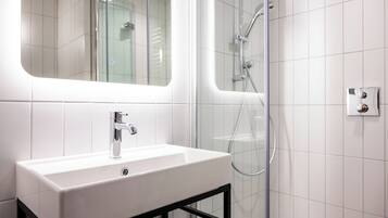 Un baño moderno con un lavamanos blanco, cerramiento de ducha de vidrio y un espejo sobre el lavamanos.