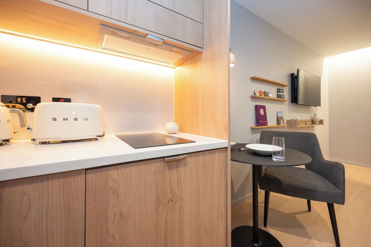 Une cuisine moderne équipée d’un grille-pain encastré, d’une tablette posée sur le plan de travail et d’une chaise devant une petite table.