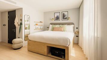 A modern bedroom with a large bed, a wooden nightstand, a mirror, and a shelf with toiletries.