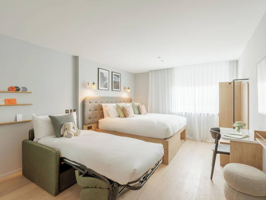 A modern hotel room with two beds, a desk, and a chair.