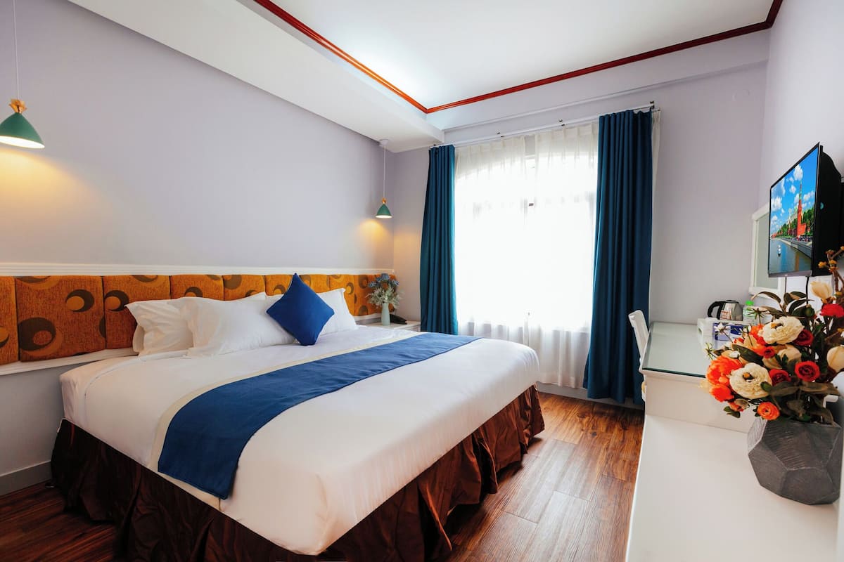 Quarto de hotel com cama, escrivaninha, televisão e janela com cortinas.