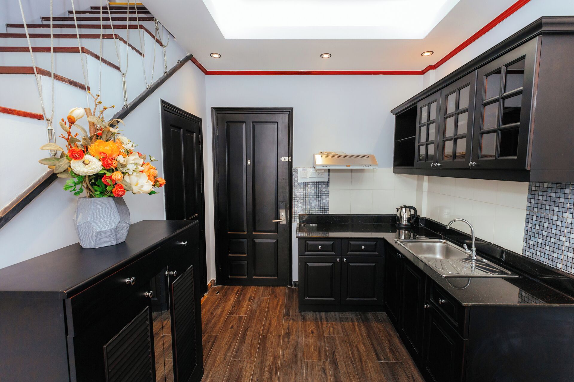 Une cuisine moderne avec des meubles de rangement noirs, un plancher en bois et une lucarne au-dessus de l’évier.