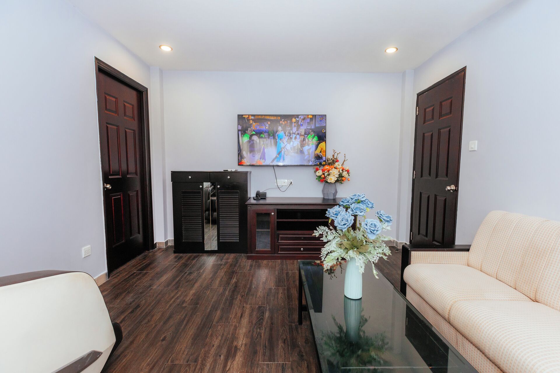 A living room with a sofa, a coffee table with a vase of flowers, a TV mounted on the wall, and a wooden cabinet.