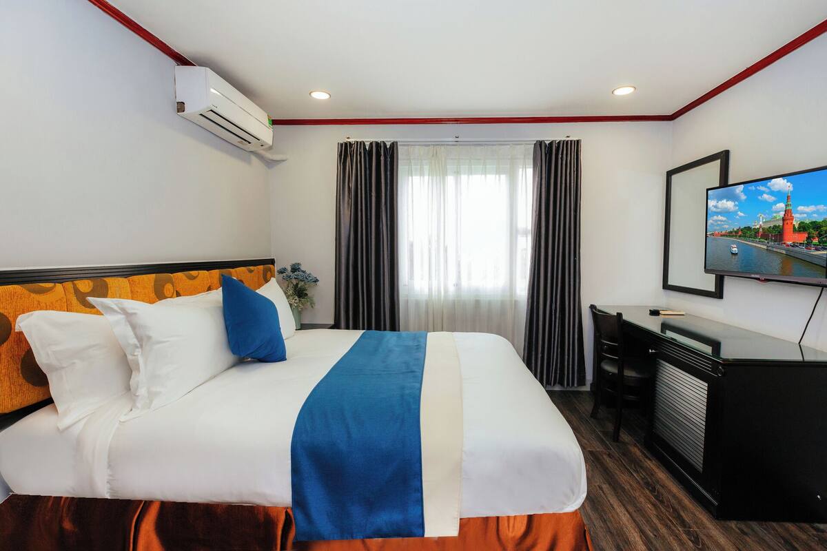 Quarto de hotel com cama, escrivaninha, televisão e ar condicionado.