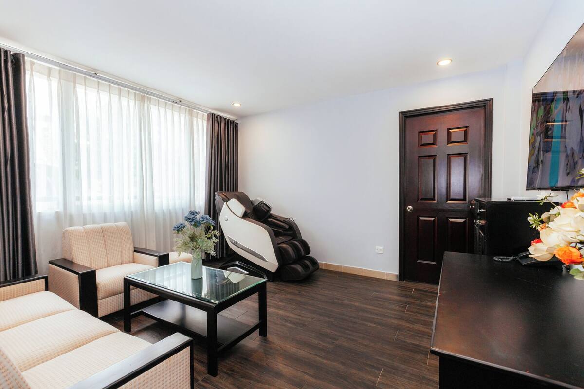 Uma sala de estar moderna com uma mesa de centro de vidro, um sofá, uma poltrona de massagem e uma porta de madeira escura.