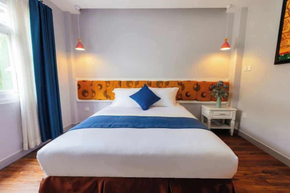 A hotel room with a large bed, two bedside lamps, a nightstand, and a window with curtains.