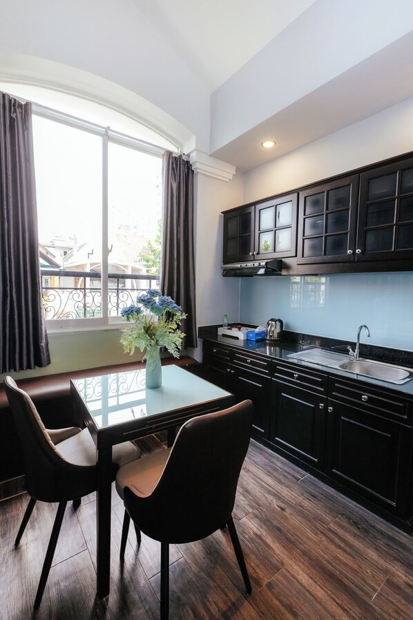 A modern kitchen with dark cabinetry, a stainless steel sink, and a dining area with two chairs and a table. - Romana Saigon Hotel Phu My Hung (Ho Chi Minh City)