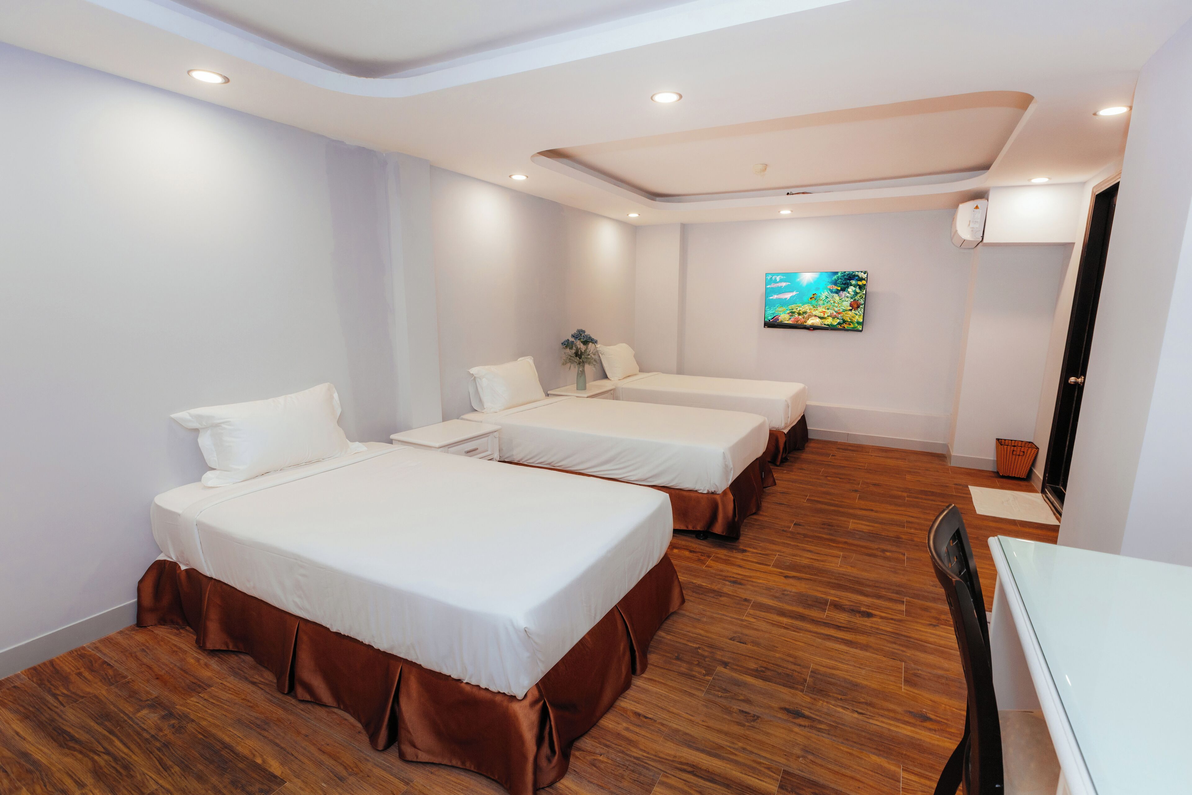 A hotel room with three single beds, a wooden floor, a white ceiling, and a painting on the wall.
