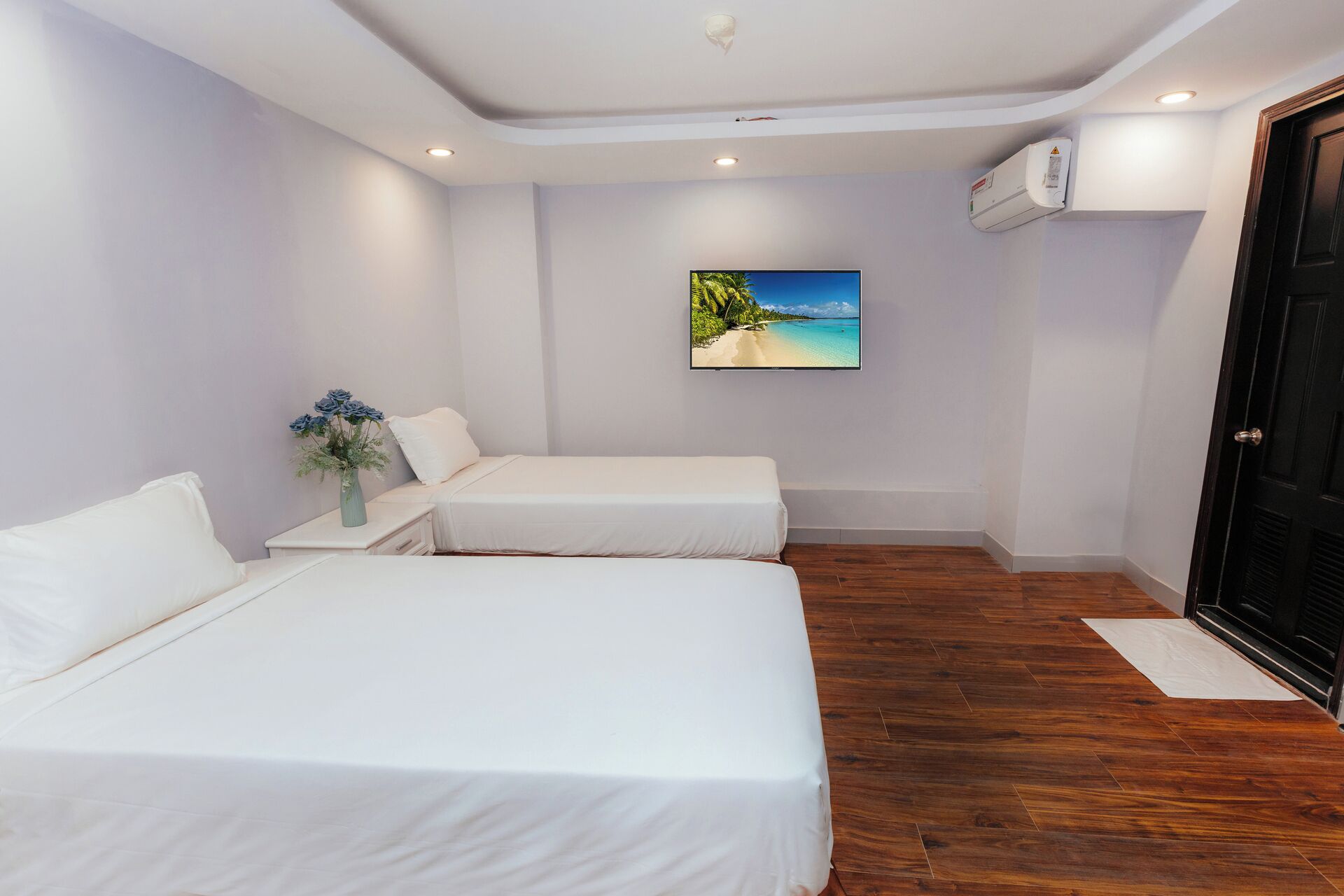 A hotel room with two single beds, a painting of a beach, an air conditioning unit, and a wooden floor.
