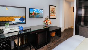 Habitación de hotel con cama, escritorio con computadora, silla, televisor y cuadros en la pared.