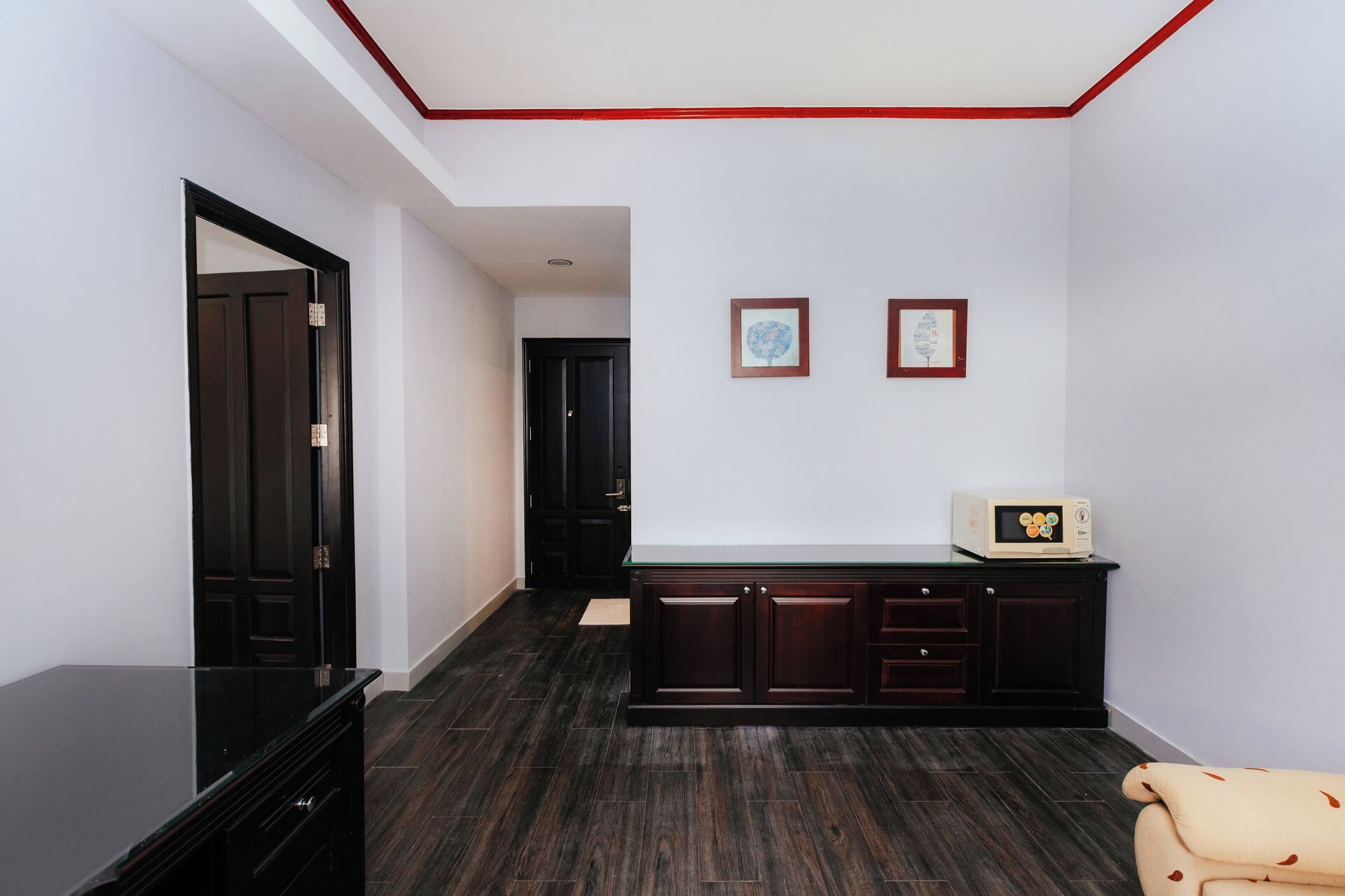 Un couloir avec un parquet en bois foncé, une commode noire et un canapé de couleur crème. Deux tableaux encadrés sont accrochés au mur.