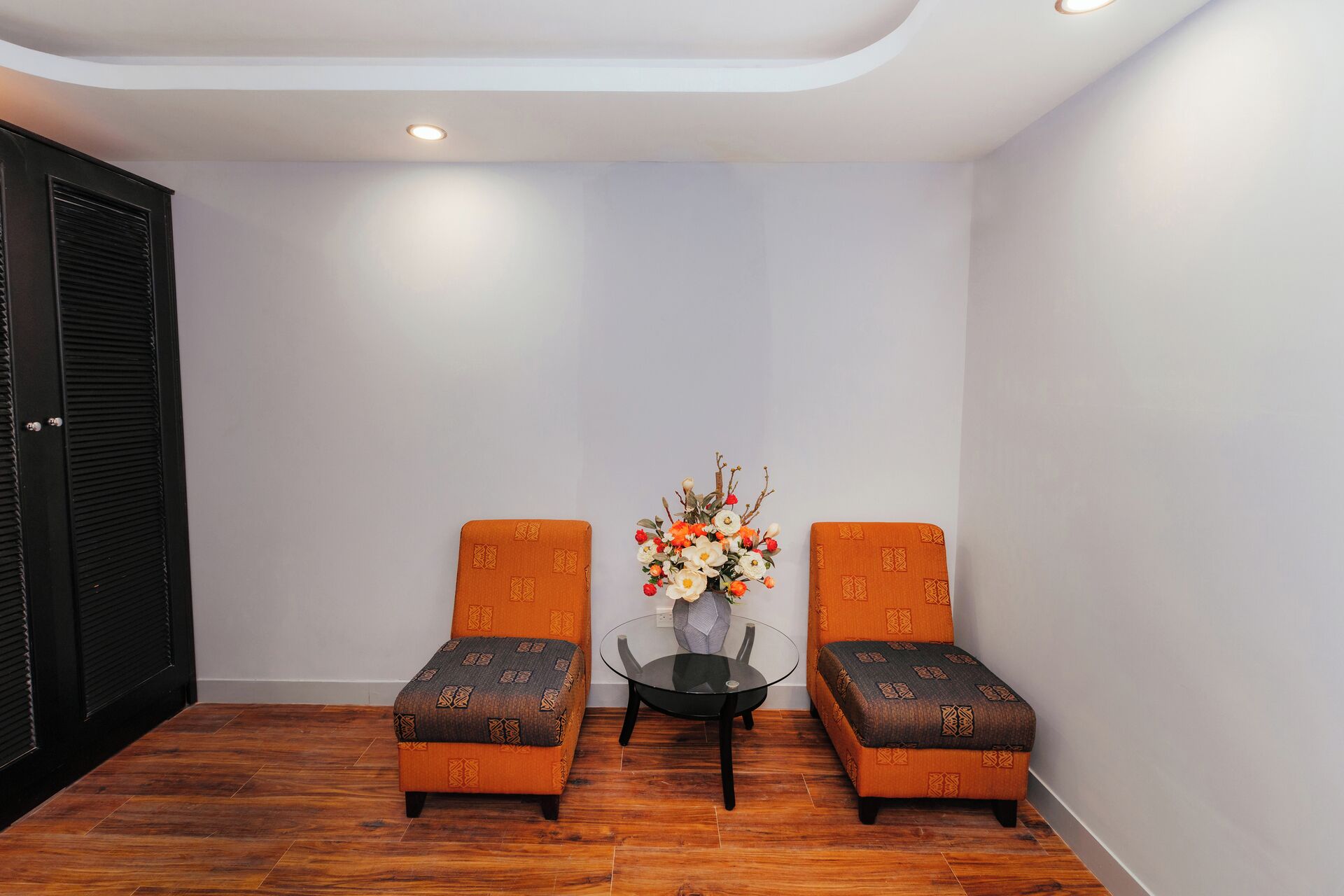 A room with two orange upholstered chairs, a glass table, and a vase with flowers.