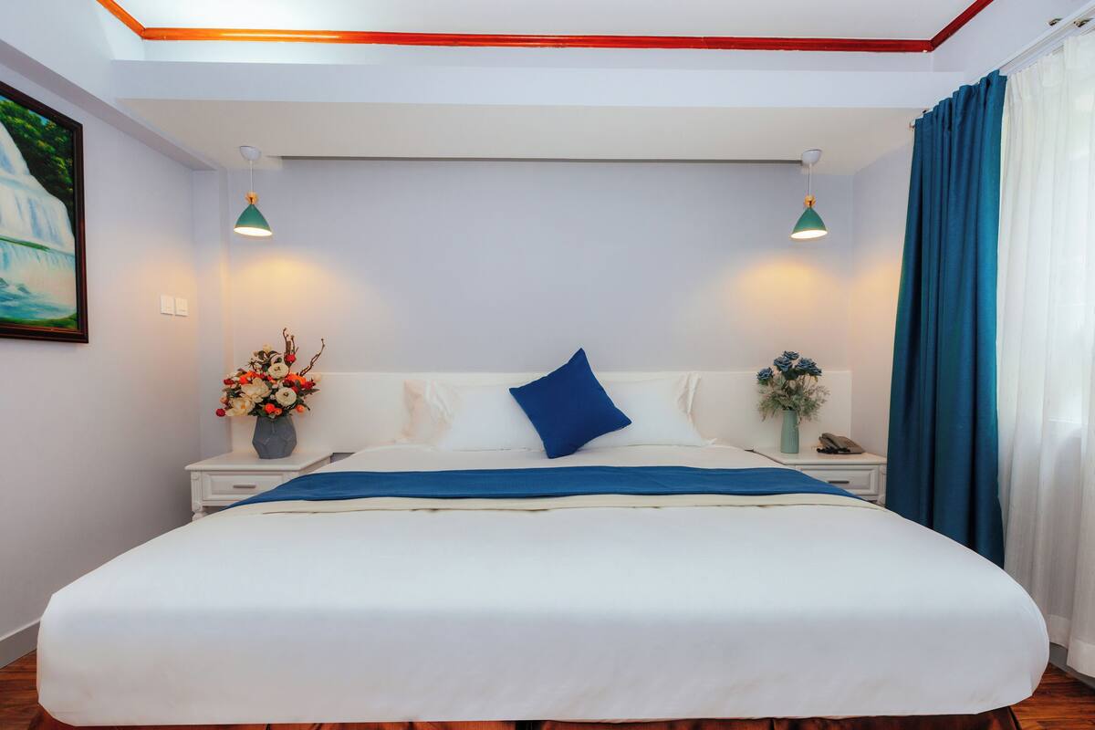 Um quarto bem arrumado com uma cama grande, mesas de cabeceira, um criado-mudo e um quadro na parede.