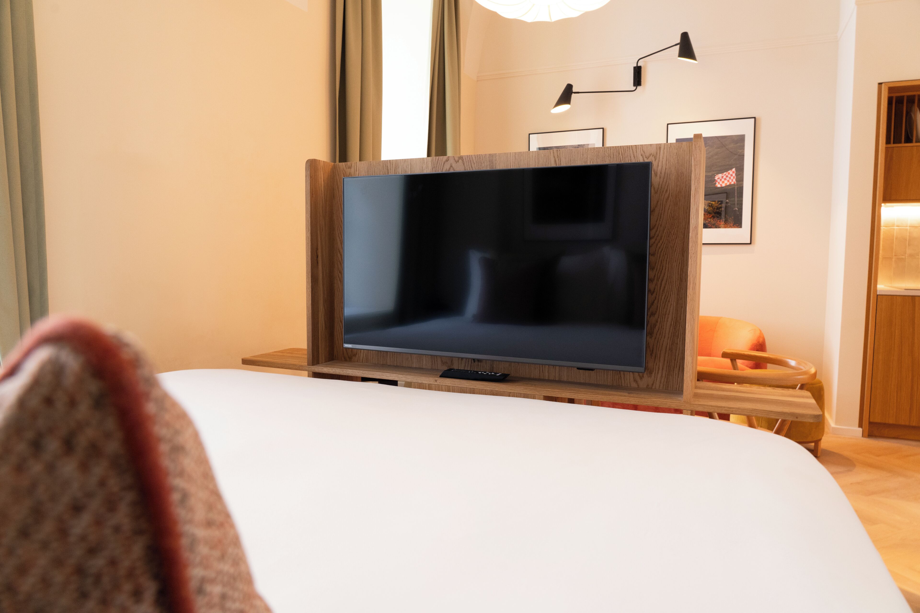 Een hotelkamer met een groot bed, een televisie op een houten standaard, een nachtkastje en een stoel.