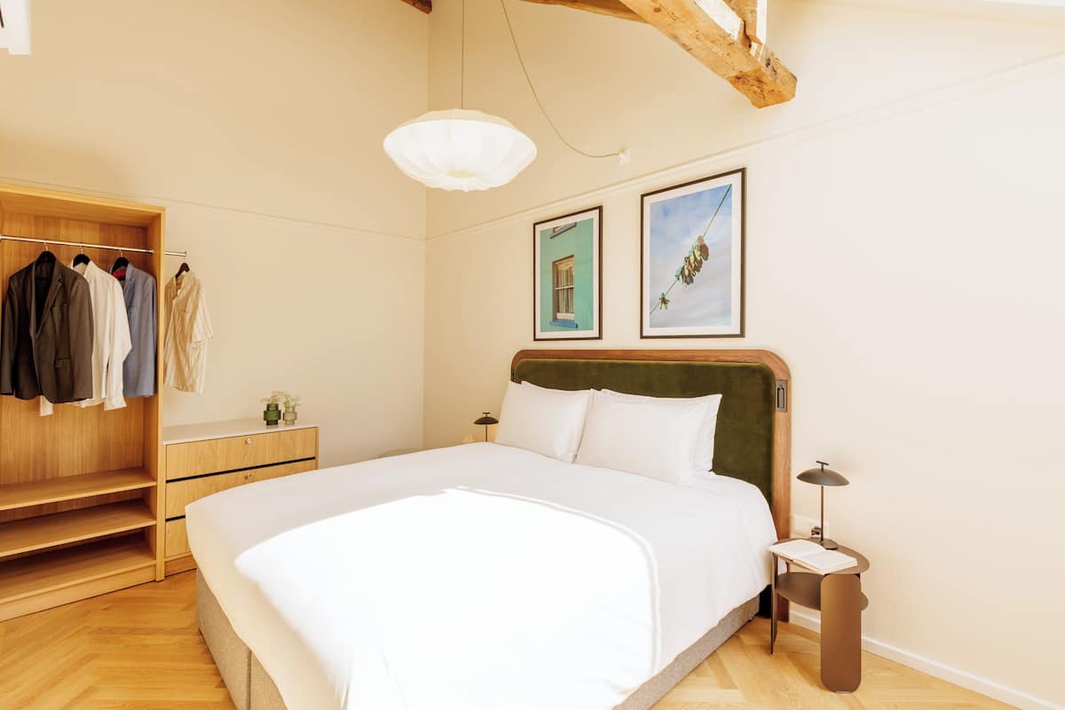 A bedroom with a large bed, wooden wardrobe, and two framed pictures on the wall.